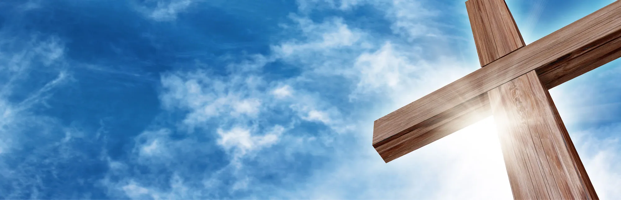 Blick von unten auf ein großes Holzkreuz vor einem leicht bewölkten Himmel